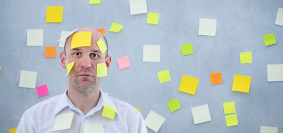 Photo of businessman overwhelmed with sticky reminder notes all around and on him